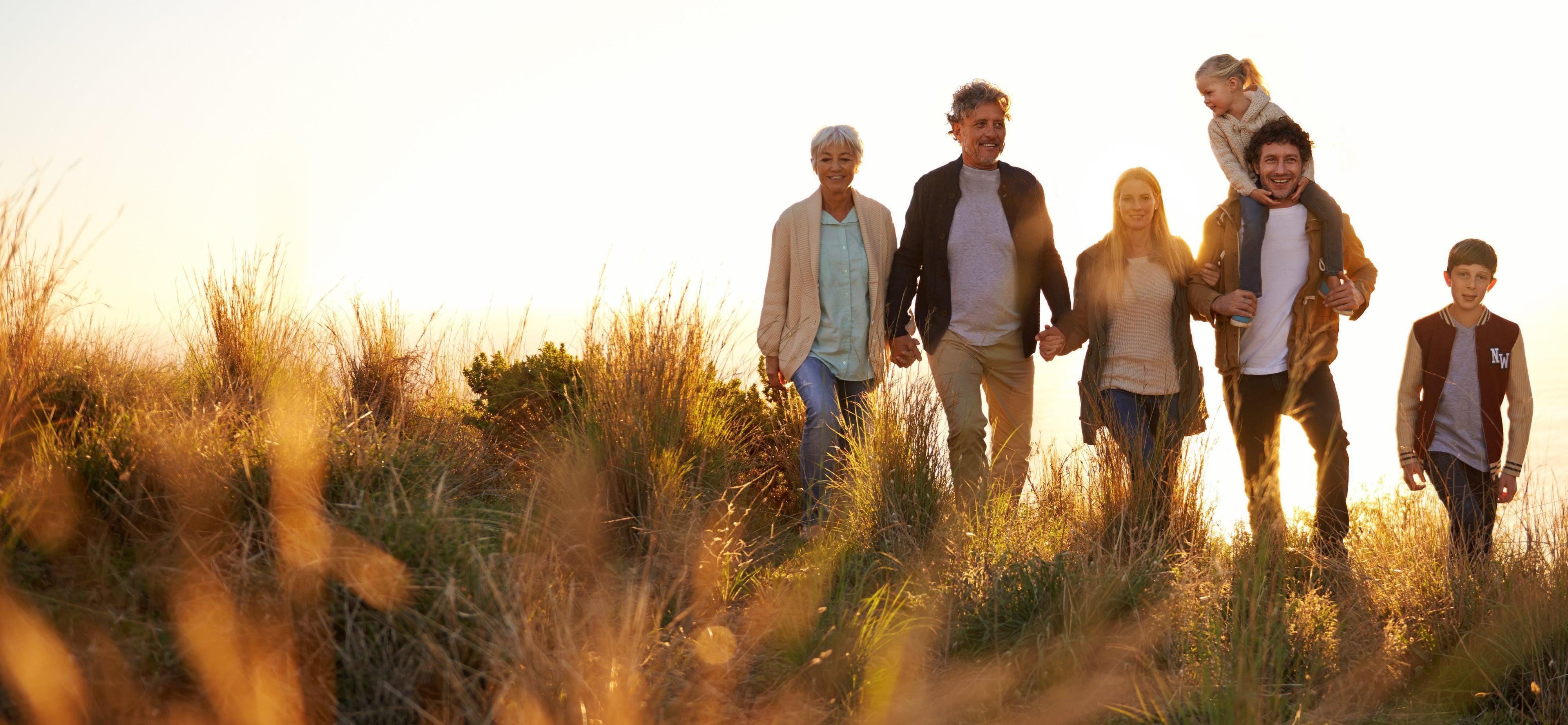 Happy family walking together at sunset, showcasing casual outfits in soft colors against a golden grassy backdrop.