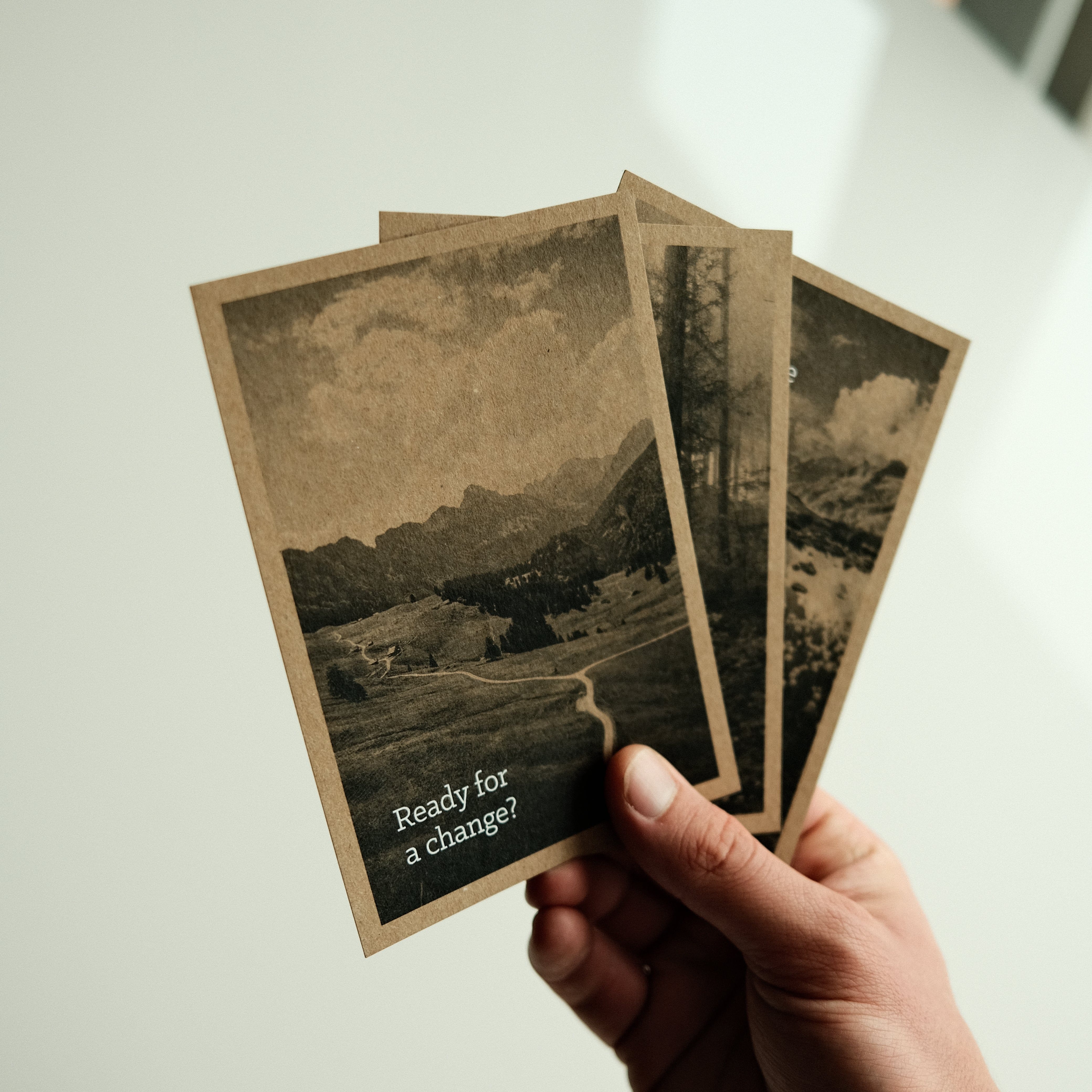 Three vintage-style postcards in sepia tones featuring scenic mountain landscapes, held in a hand.