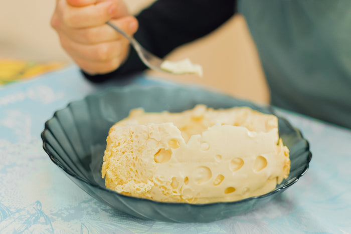 一个长相欧洲人的男孩坐在桌边吃早餐，他用叉子吃乳制品，表情丰富。食物概念 