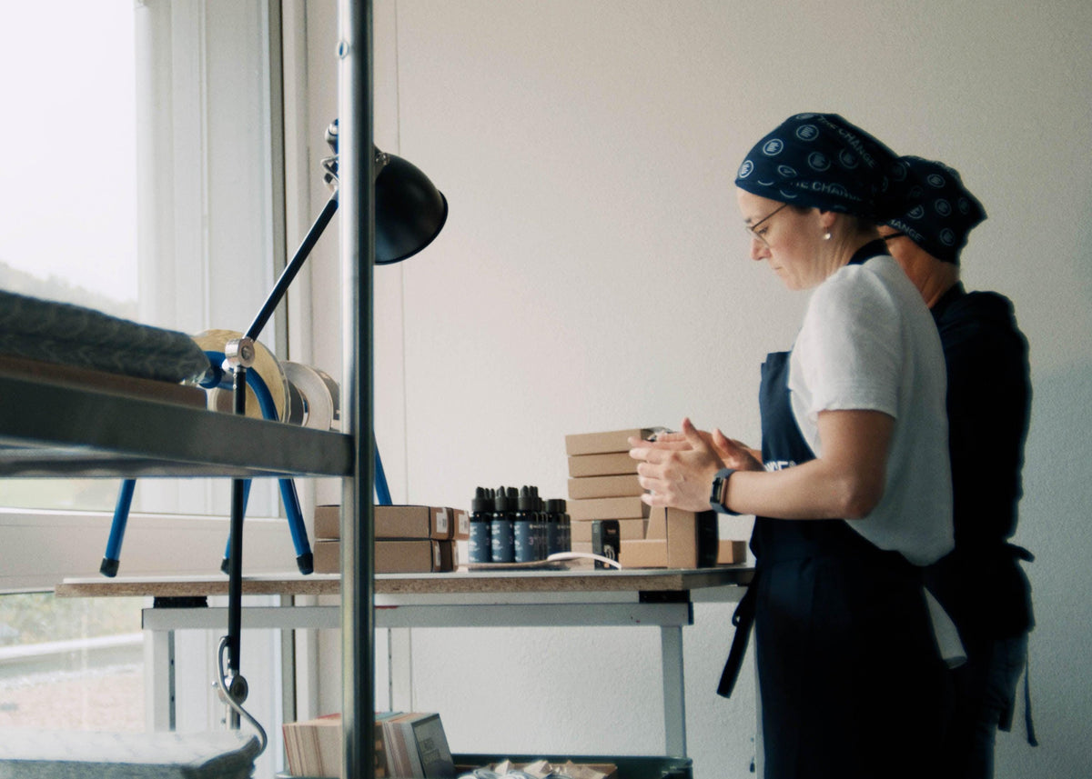 Women in blue bandanas packing eco-friendly skincare products in minimalist workspace with natural light.