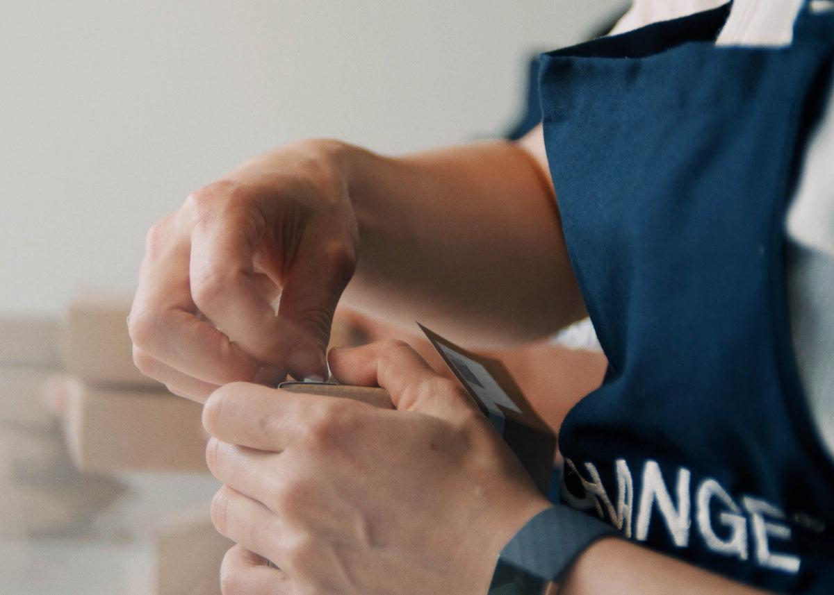 Blue apron-clad hands open a product package, showcasing a modern, minimalist style.